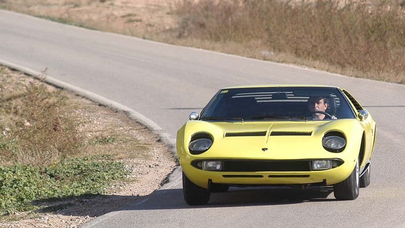 Yellow Lamborghini Miura on a rural road, the mid-engined V12 design icon that invented the supercar template.